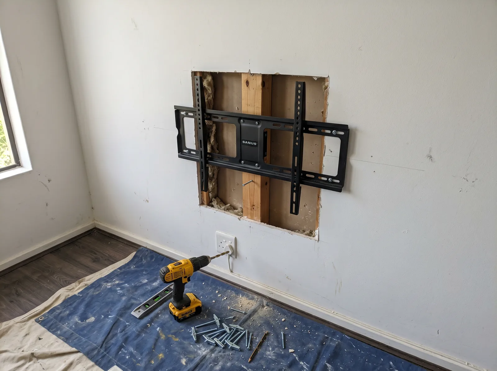 TV wall-mount bracket fixed to a gypsum drywall wall with the cavity opened to show timber studs and toggle bolts, Gauteng home