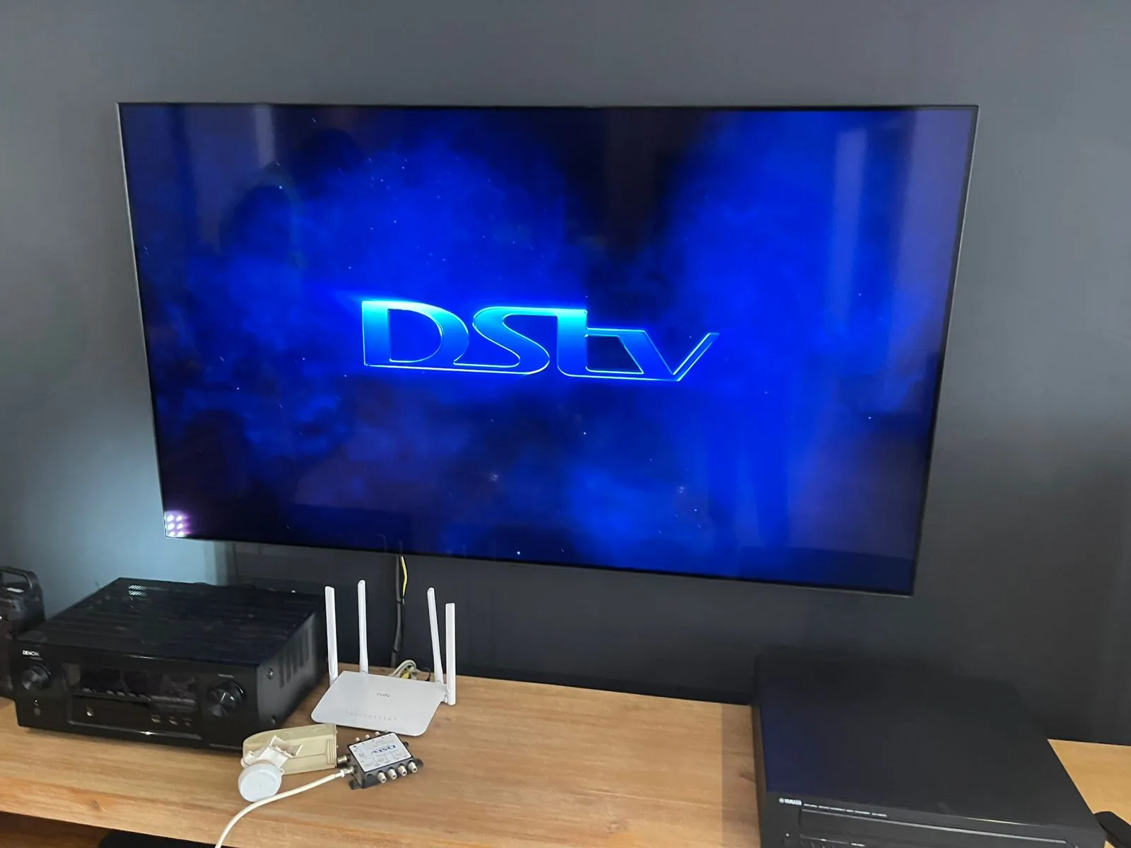 Home theatre setup with a large TV, DSTV decoder, amplifier and router