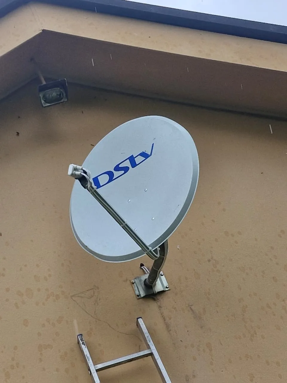 DSTV satellite dish installation in progress with ladder against an orange wall