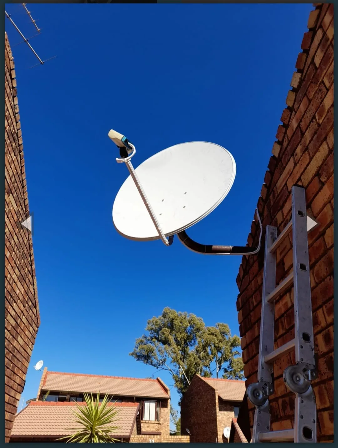 DSTV satellite dish mounted between two townhouse brick walls under clear sky