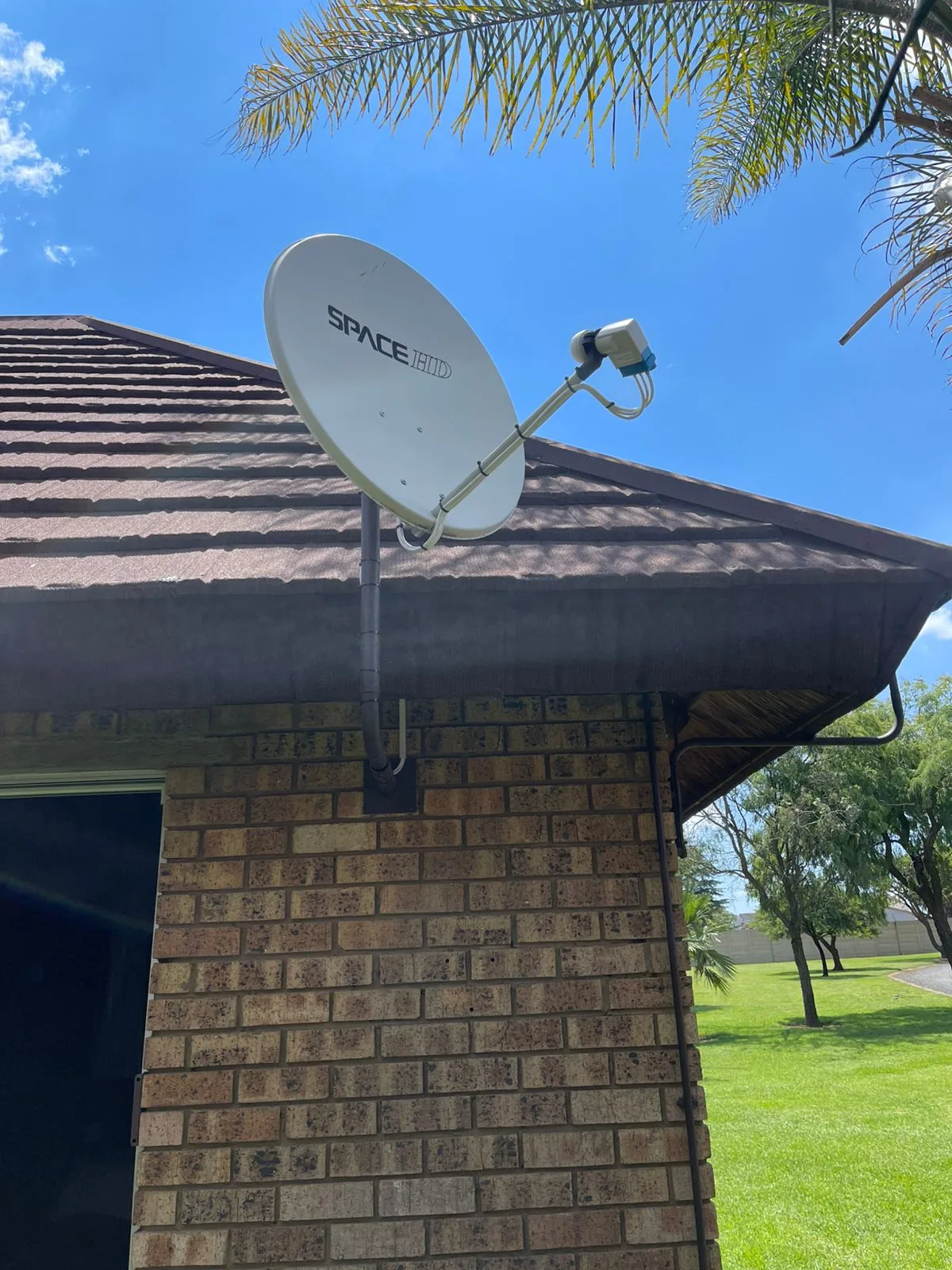 DSTV Space HD satellite dish mounted on a face-brick home with a palm tree